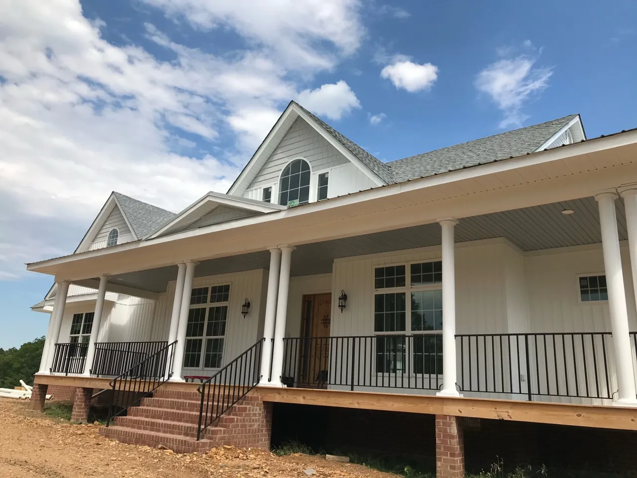 White farmhouse with a wraparound porch, columns and brick steps